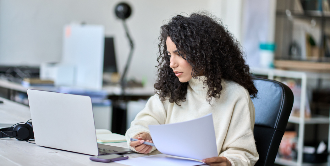 Woman looking at a laptop with papers in her hand.